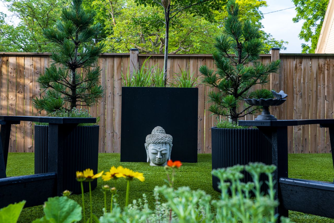 Peaceful garden scene featuring Buddha head sculpture and lush green plants.